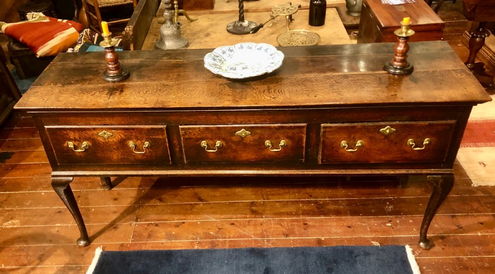 An 18th-century dark oak dresser base featuring three brass-handled drawers supported on slender cabriole legs.