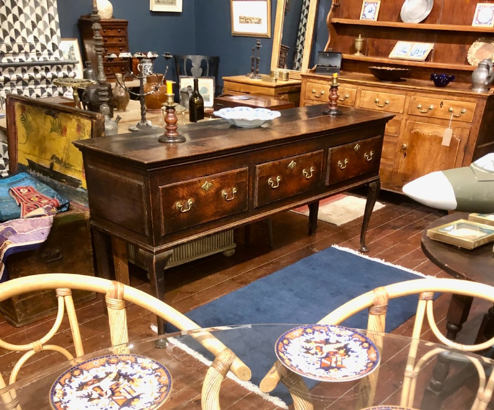 An 18th-century dark oak dresser base featuring three brass-handled drawers supported on slender cabriole legs. View VII