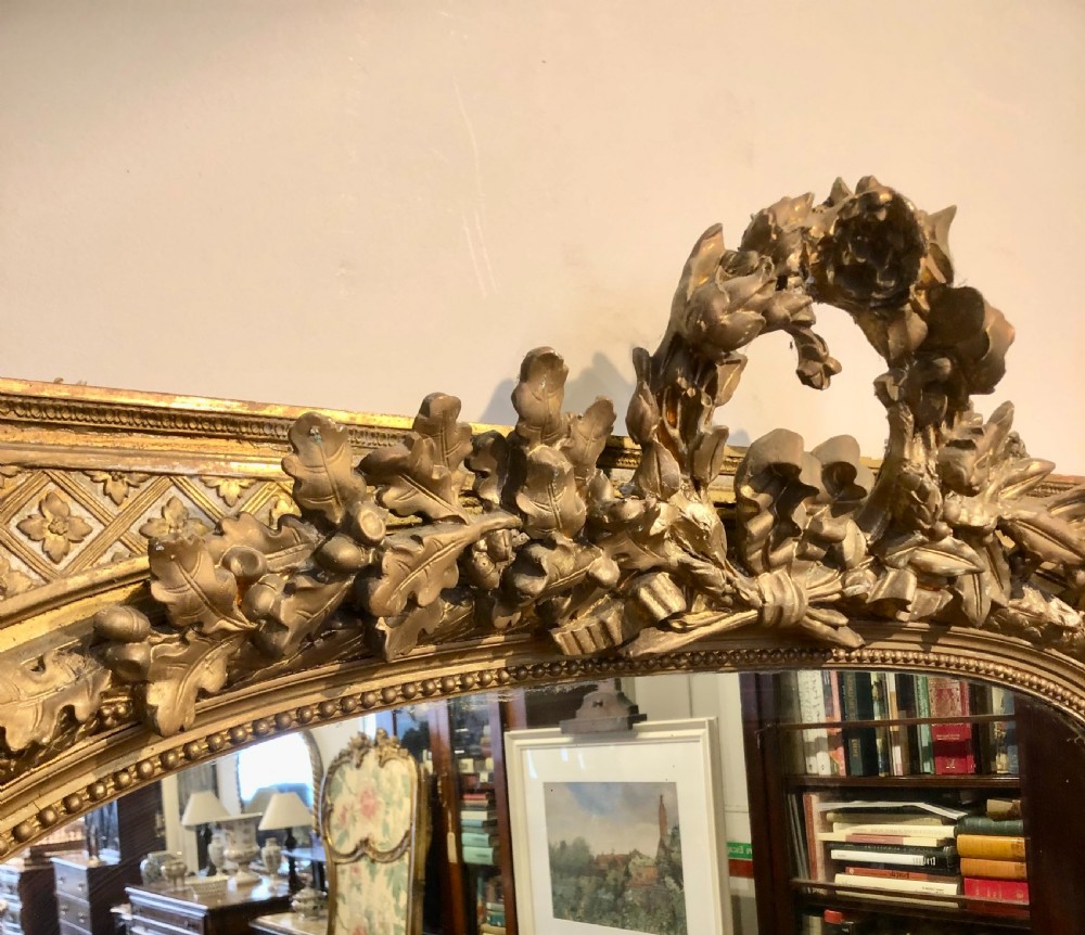 A large rectangular French giltwood wall mirror featuring an arched inner frame with floral cresting and carved decorative borders. View V