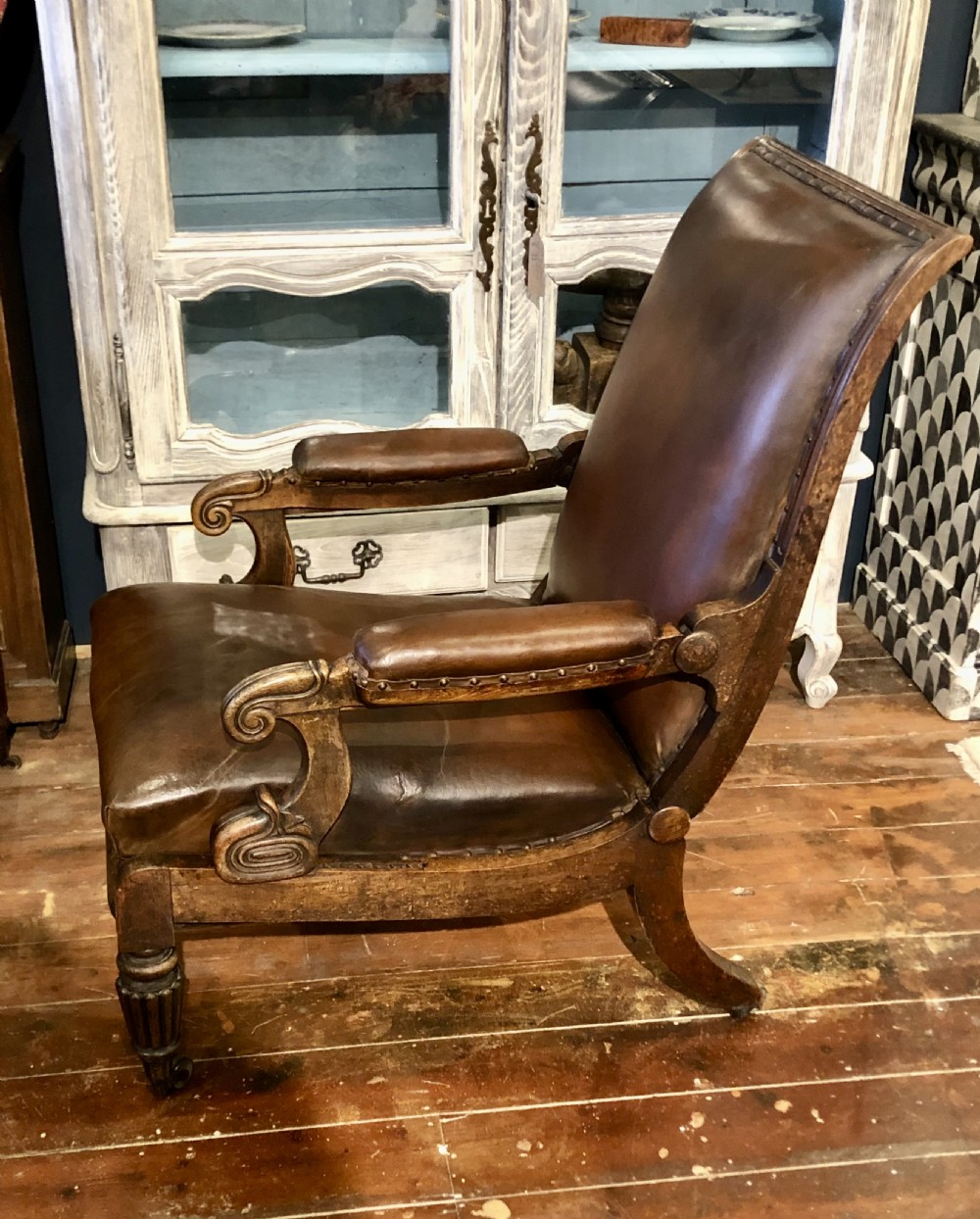 A Regency mahogany library armchair upholstered in warm brown leather with scroll arms, reeded front legs, brass castors, and studding. View II