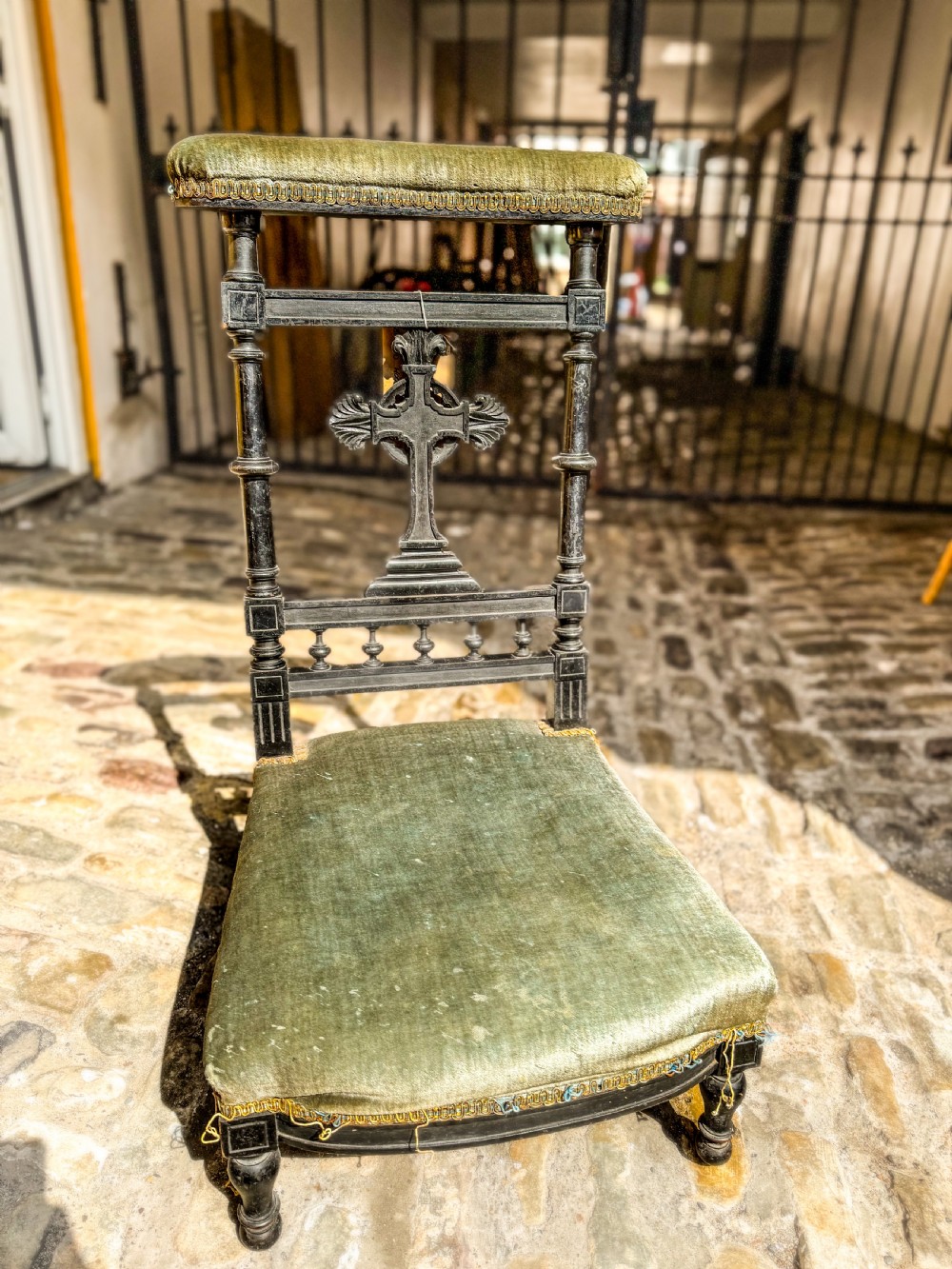 A 19th-century ebonised wood prie-dieu prayer chair featuring a carved central cross, turned upright spindles, and sage green velvet upholstery on the kneeling seat and top rail.