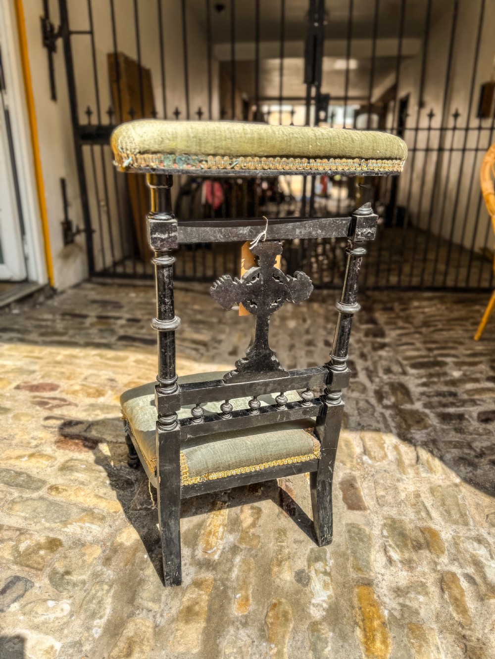 A 19th-century ebonised wood prie-dieu prayer chair featuring a carved central cross, turned upright spindles, and sage green velvet upholstery on the kneeling seat and top rail. View III