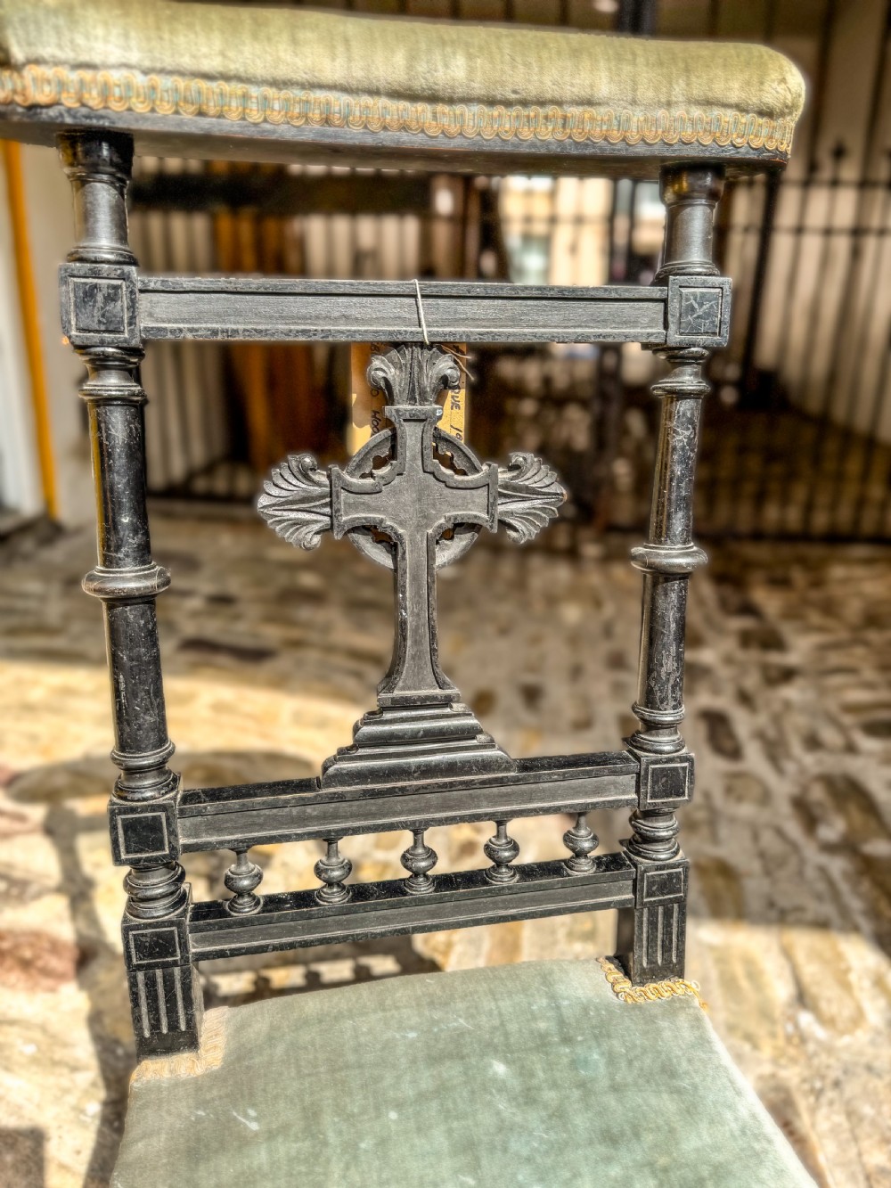 A 19th-century ebonised wood prie-dieu prayer chair featuring a carved central cross, turned upright spindles, and sage green velvet upholstery on the kneeling seat and top rail. View V