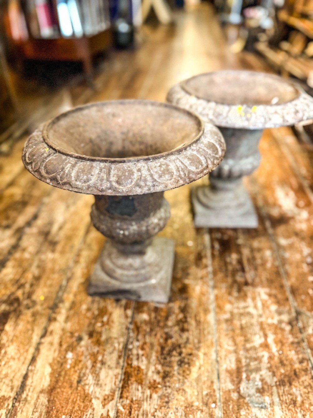 A pair of weathered Victorian cast iron garden urns featuring egg-and-dart moulded rims and square pedestal bases.