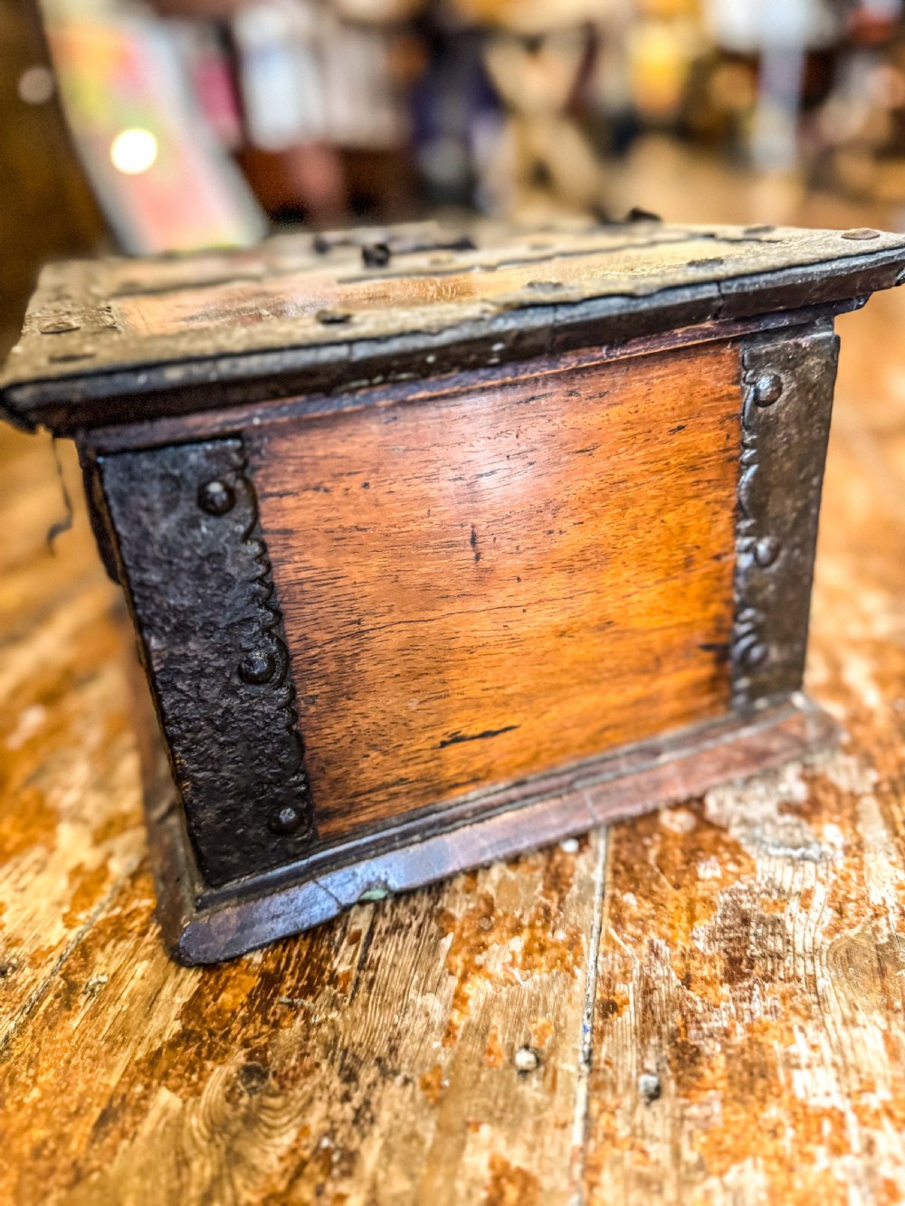 A 17th-century rectangular wooden box featuring heavy wrought-iron corner braces, decorative straps, a top carrying handle, and an oversized front lockplate. View IV
