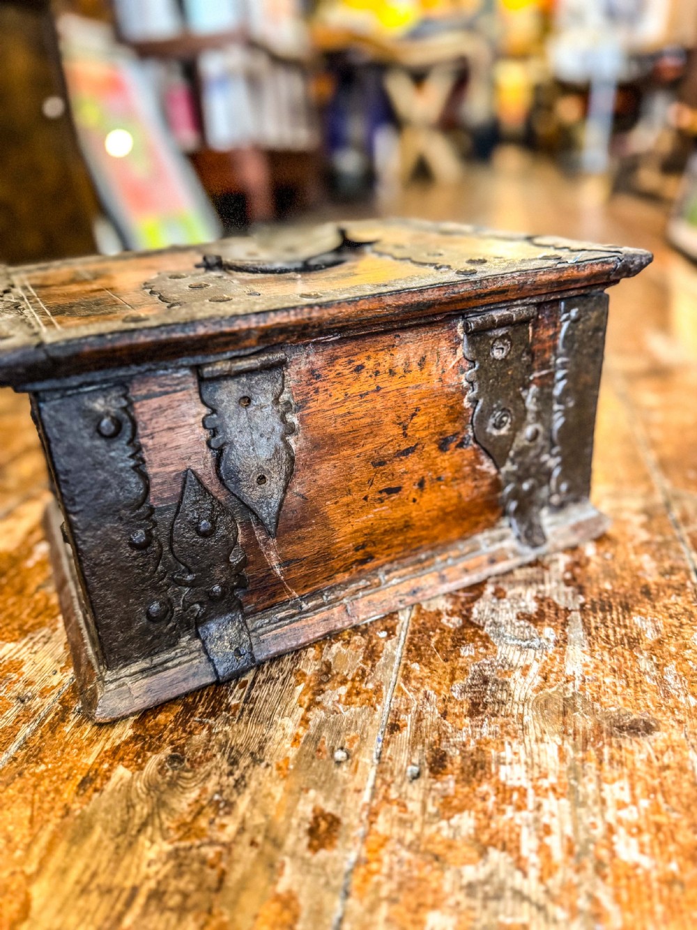 A 17th-century rectangular wooden box featuring heavy wrought-iron corner braces, decorative straps, a top carrying handle, and an oversized front lockplate. View V