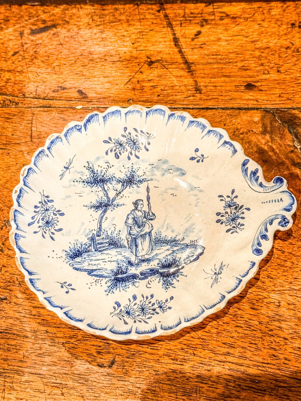 A nineteenth-century French blue and white faience shell-shaped vide-poche dish decorated with a central figure, floral sprigs, and a scalloped rim.