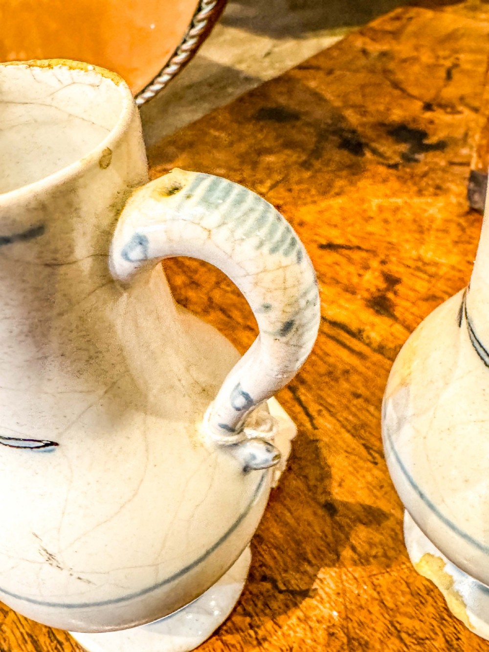 A pair of small antique off-white tin-glazed earthenware jugs decorated with hand-painted blue floral motifs on pedestal bases. View II
