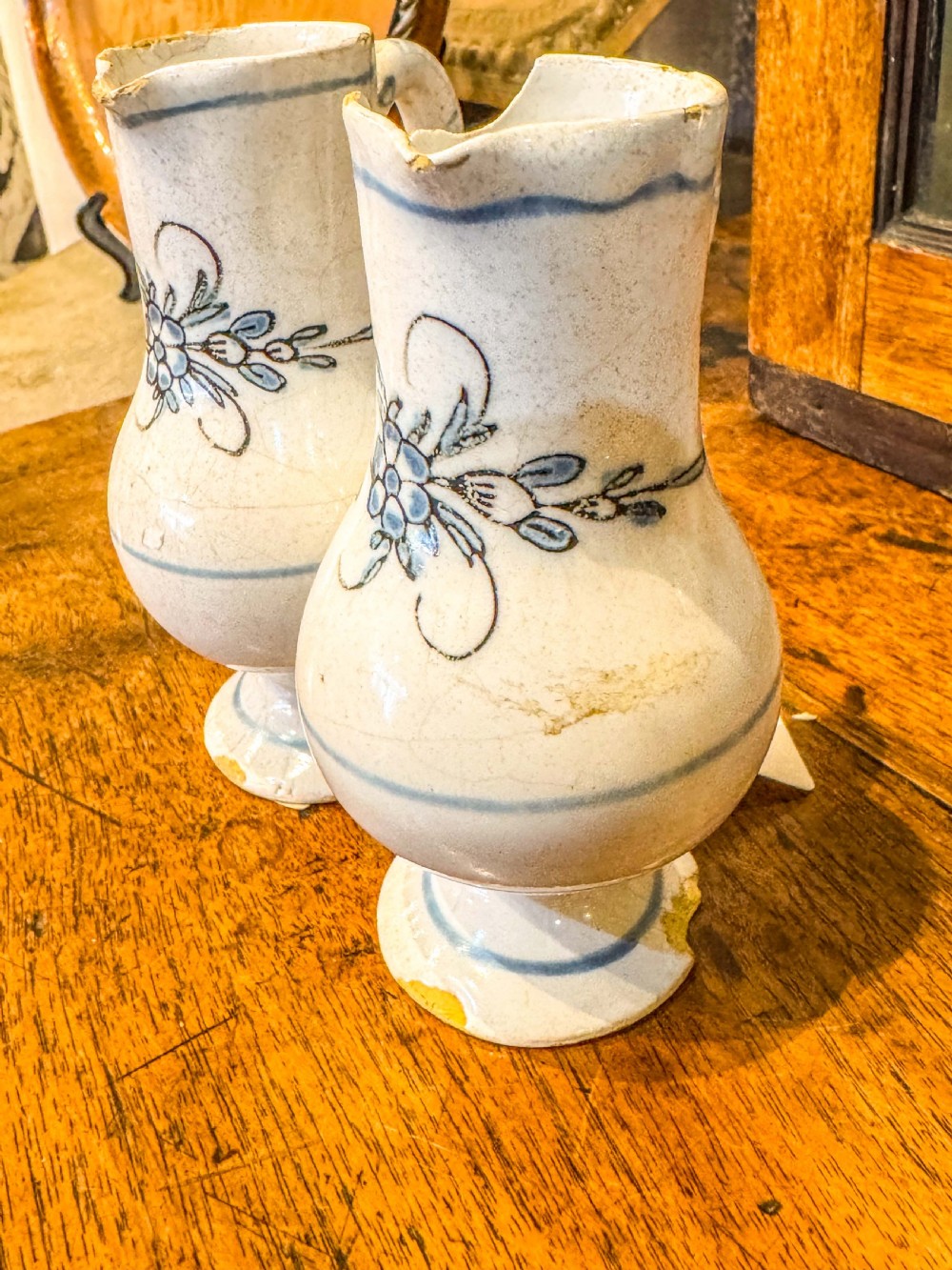 A pair of small antique off-white tin-glazed earthenware jugs decorated with hand-painted blue floral motifs on pedestal bases. View IV