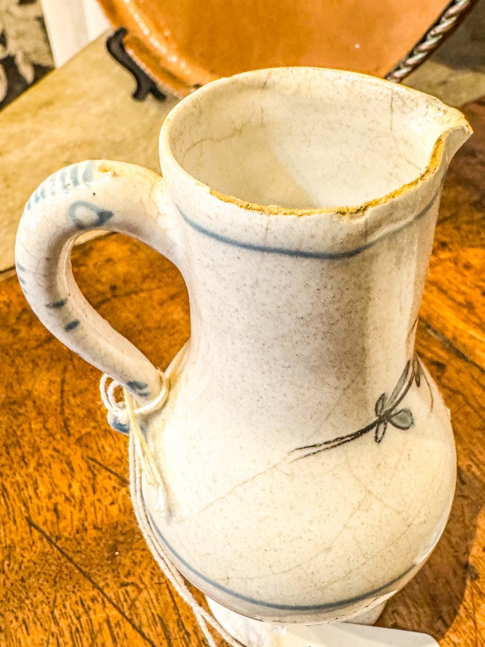 A pair of small antique off-white tin-glazed earthenware jugs decorated with hand-painted blue floral motifs on pedestal bases. View V