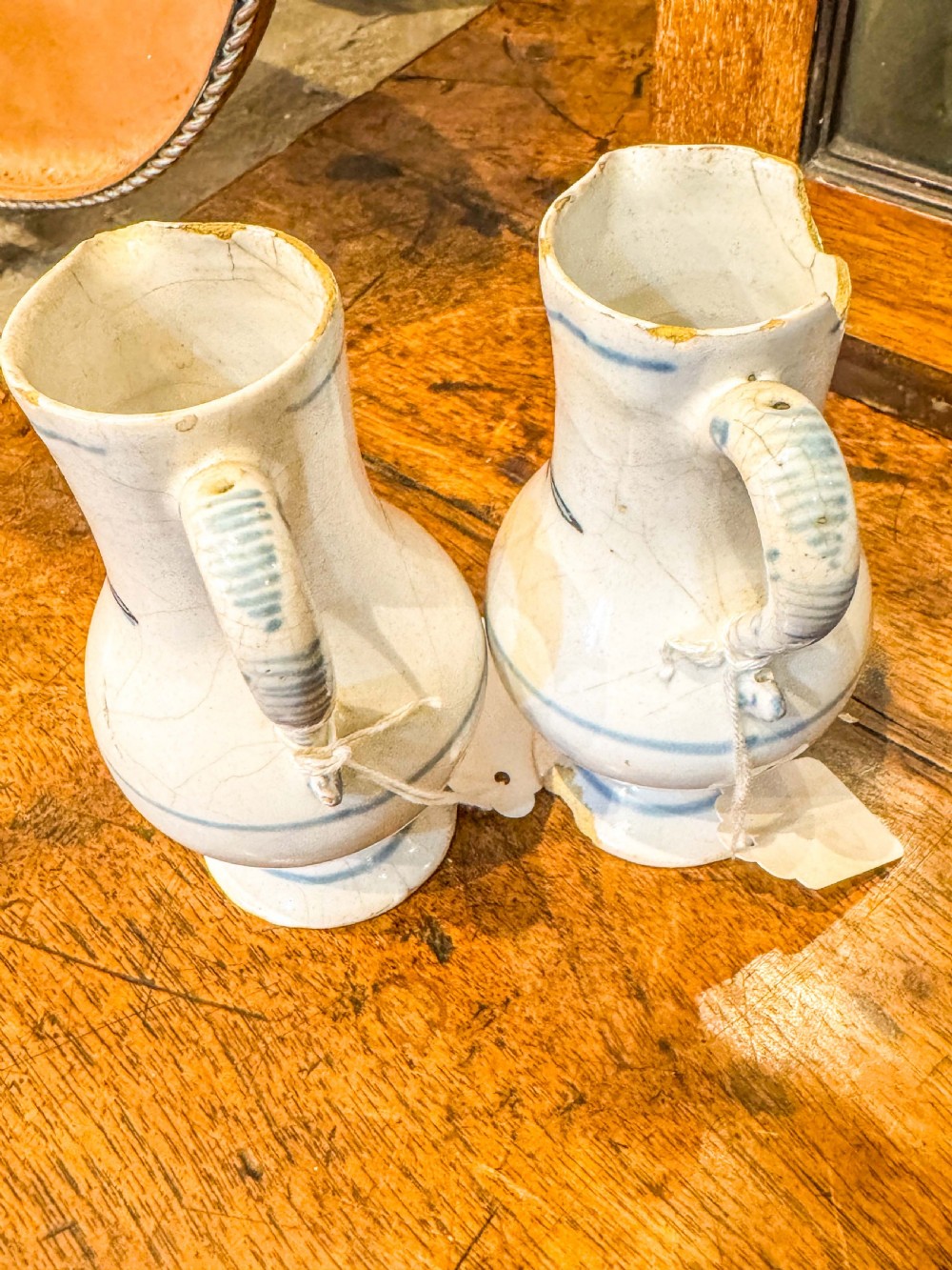 A pair of small antique off-white tin-glazed earthenware jugs decorated with hand-painted blue floral motifs on pedestal bases. View VI