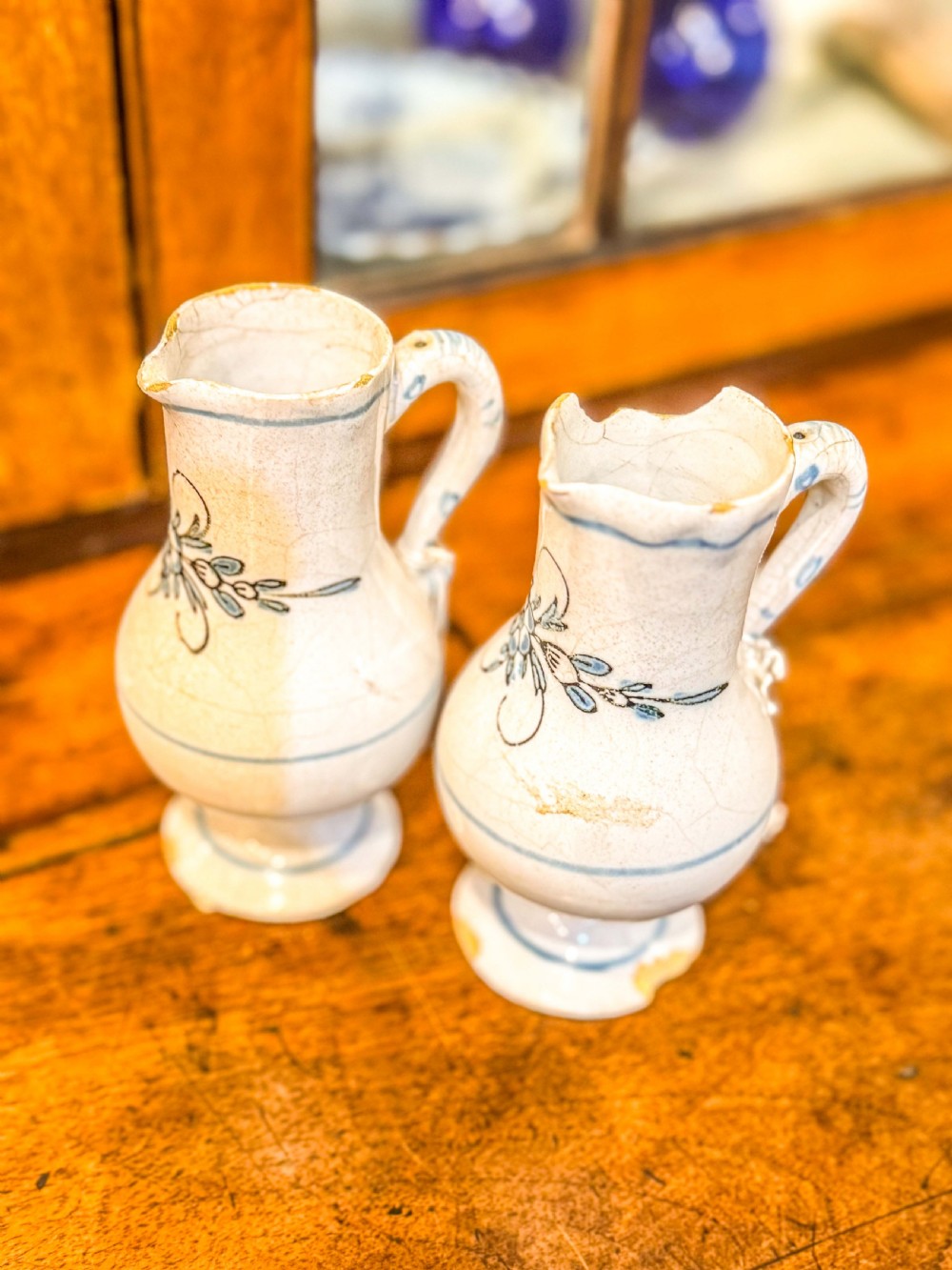 A pair of small antique off-white tin-glazed earthenware jugs decorated with hand-painted blue floral motifs on pedestal bases. View VII