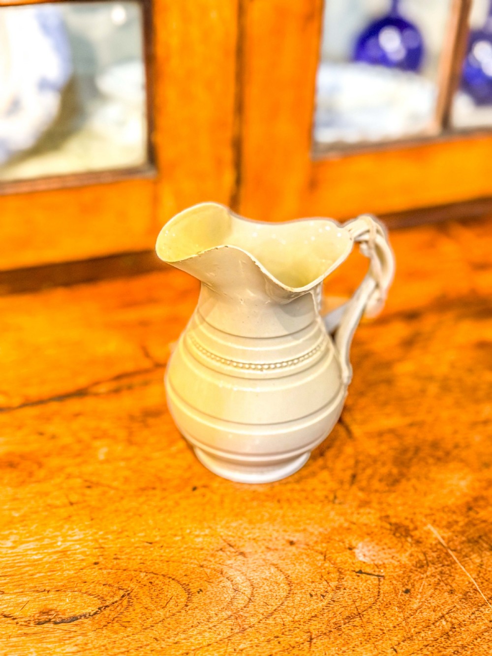 An 18th-century creamware pottery milk jug featuring moulded ribbed bands, a flared spout, and a looped handle.