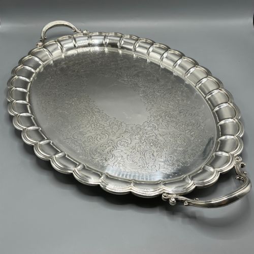 fig 1. A large oval silver plated serving tray featuring twin scroll handles, a scalloped rim, and chased foliage patterns across the flat interior.