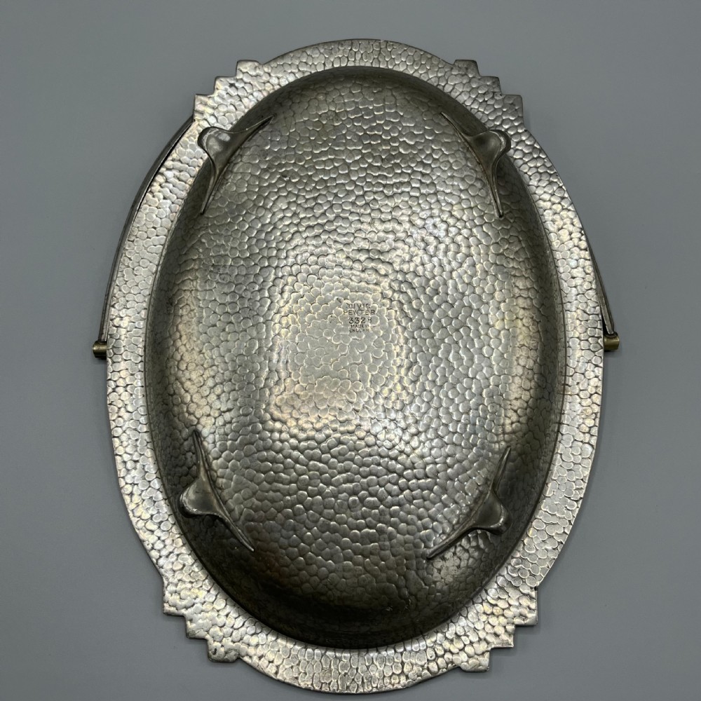 An oval hand-hammered pewter fruit basket featuring a high arching handle, geometric rim details, and small cast feet. View XI
