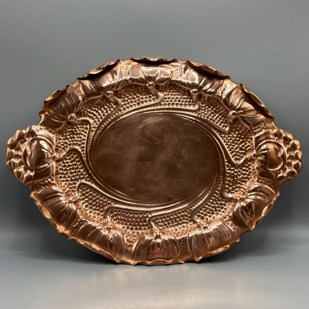 An oval Art Nouveau copper tray with hand-punched background texturing, scalloped edges, and embossed floral relief motifs.