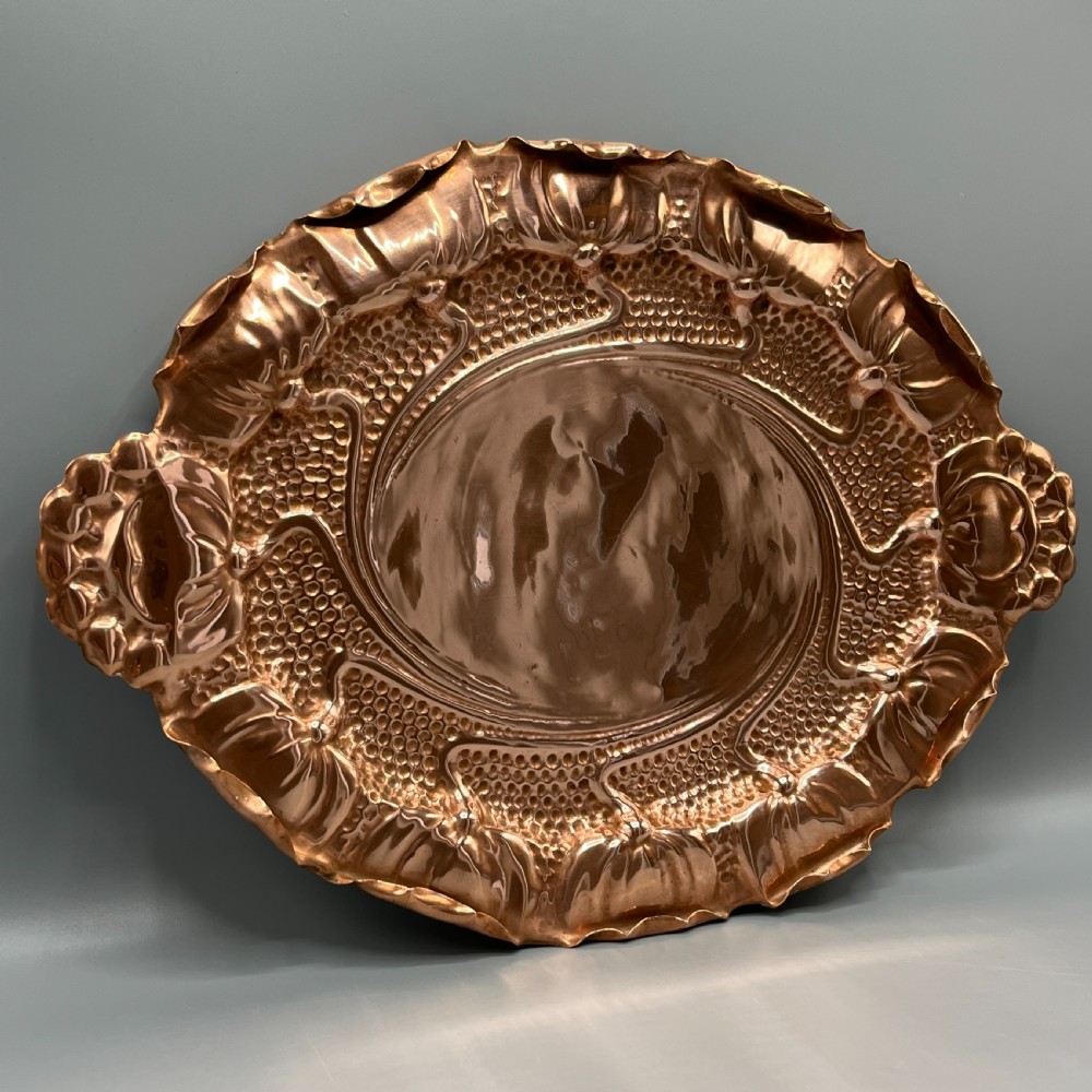 An oval Art Nouveau copper tray with hand-punched background texturing, scalloped edges, and embossed floral relief motifs. View II