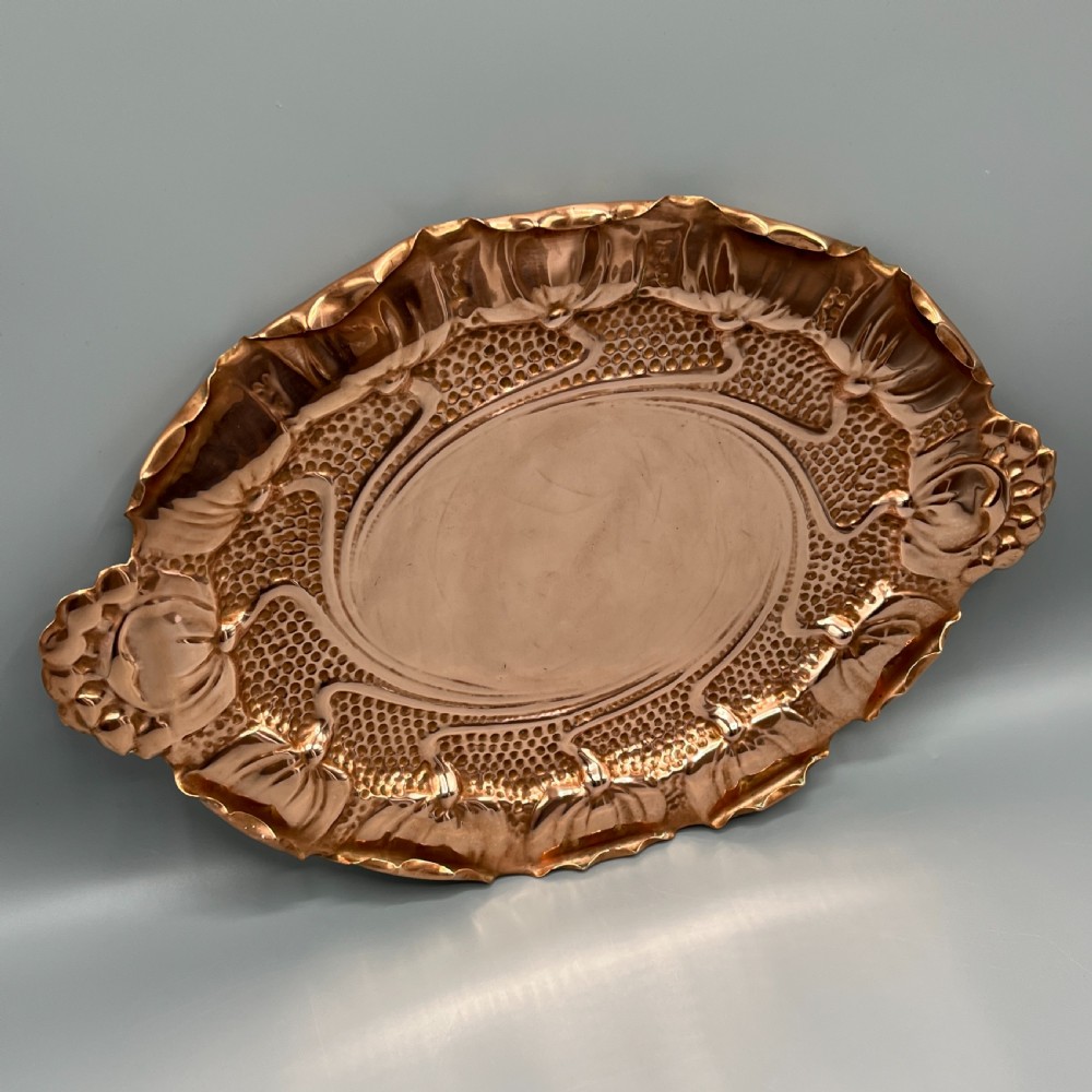 An oval Art Nouveau copper tray with hand-punched background texturing, scalloped edges, and embossed floral relief motifs. View III