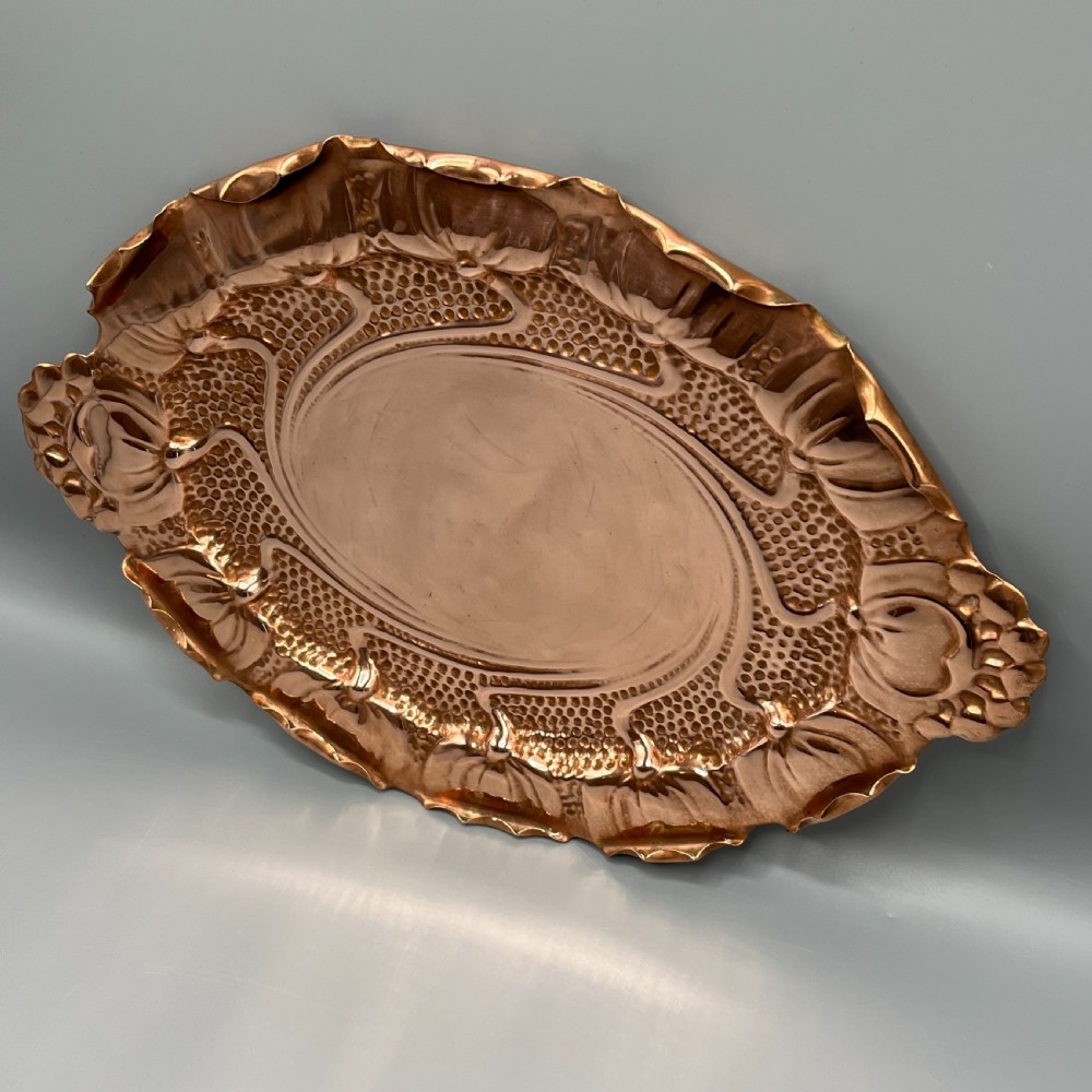 An oval Art Nouveau copper tray with hand-punched background texturing, scalloped edges, and embossed floral relief motifs. View IV
