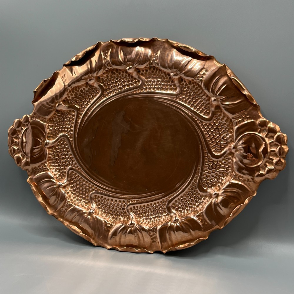 An oval Art Nouveau copper tray with hand-punched background texturing, scalloped edges, and embossed floral relief motifs. View V