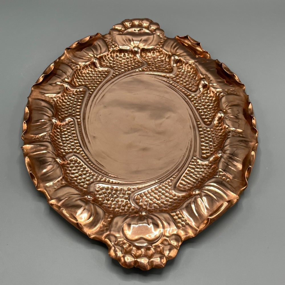 An oval Art Nouveau copper tray with hand-punched background texturing, scalloped edges, and embossed floral relief motifs. View VI