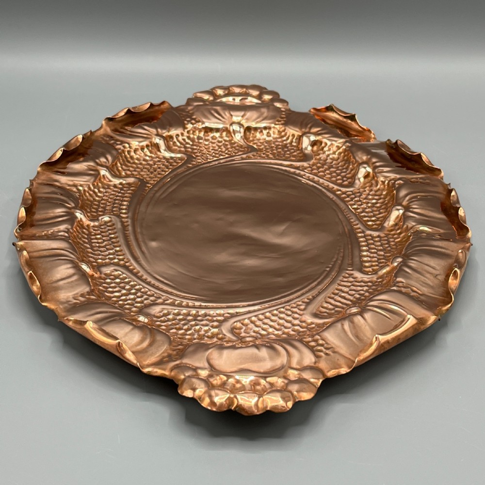 An oval Art Nouveau copper tray with hand-punched background texturing, scalloped edges, and embossed floral relief motifs. View VII