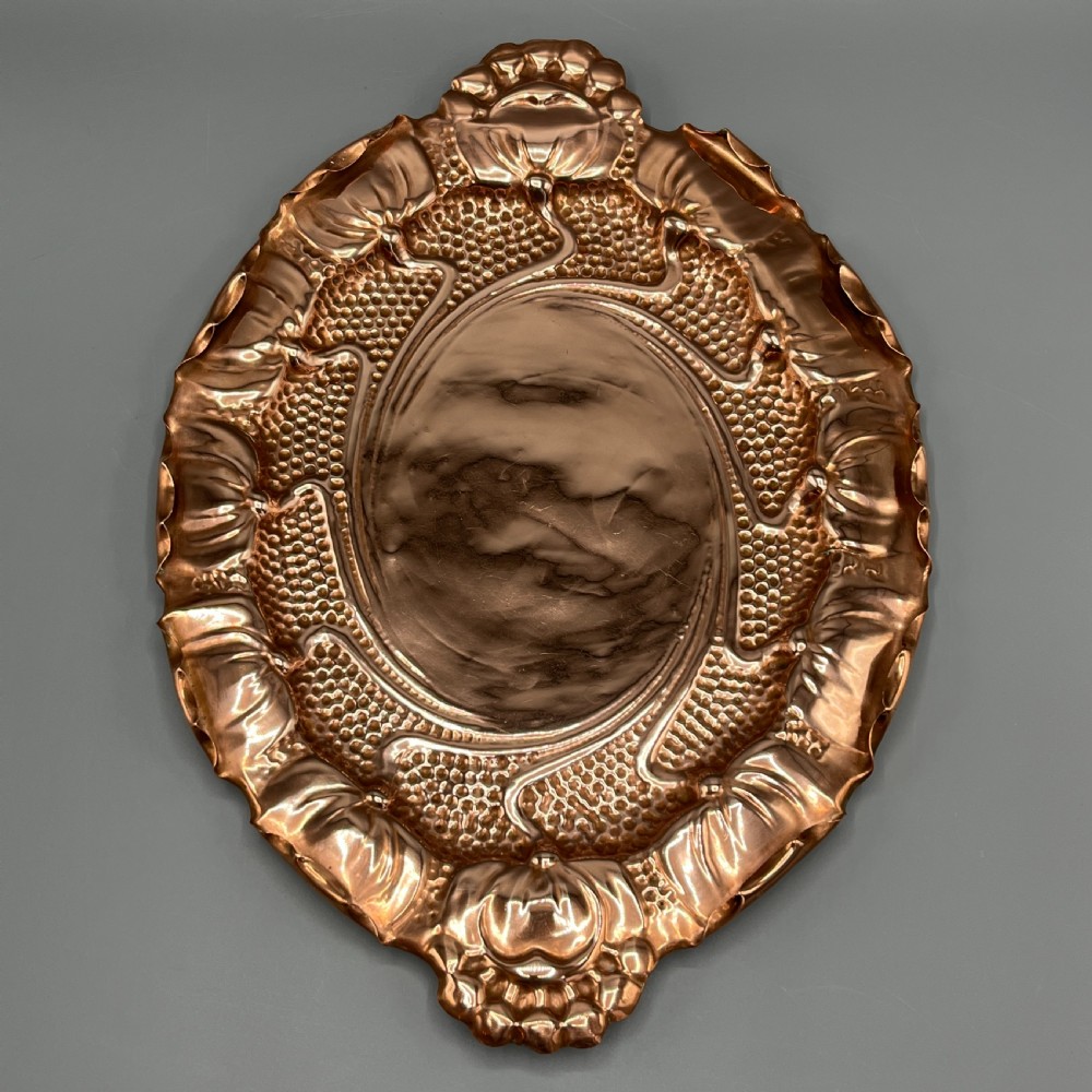 An oval Art Nouveau copper tray with hand-punched background texturing, scalloped edges, and embossed floral relief motifs. View VIII