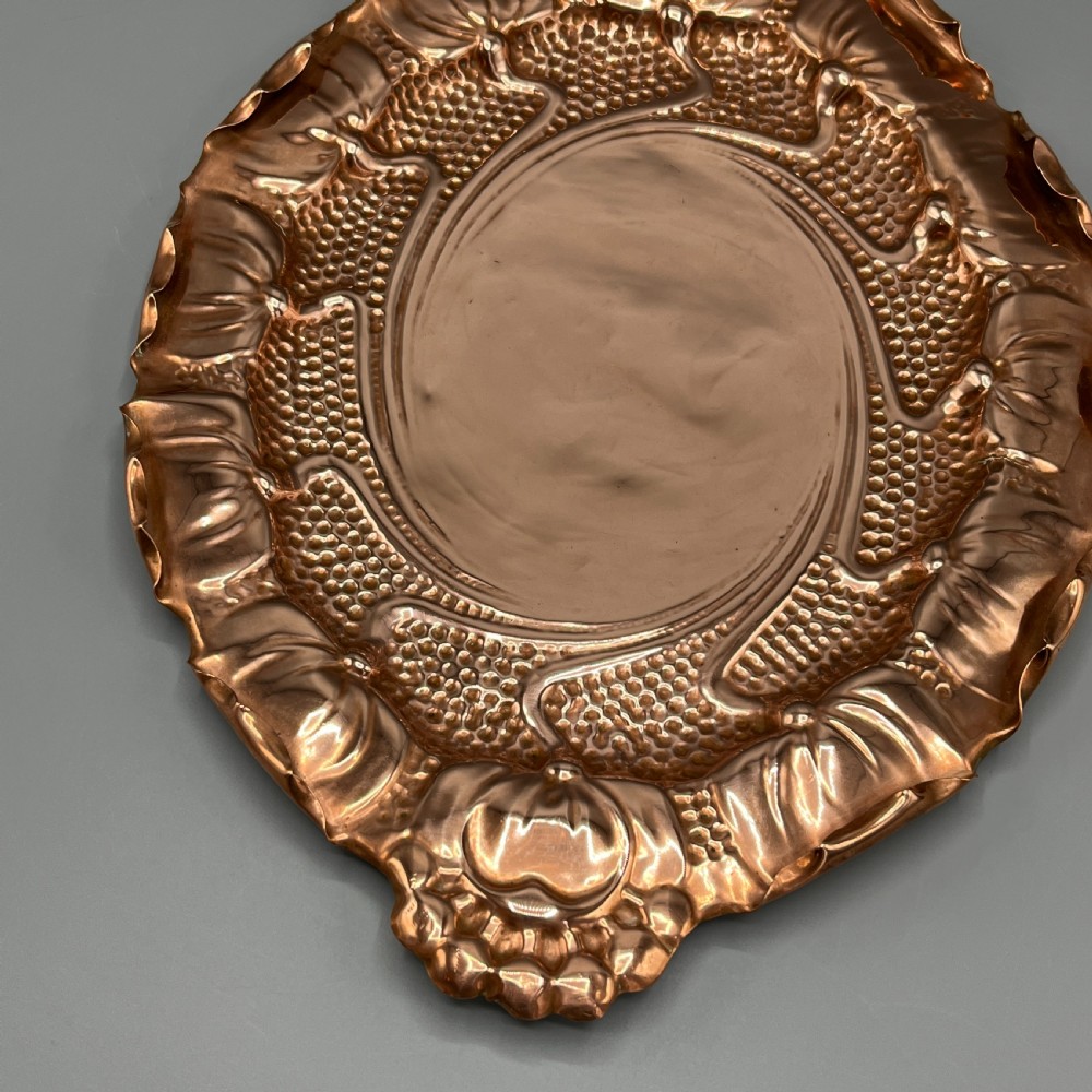 An oval Art Nouveau copper tray with hand-punched background texturing, scalloped edges, and embossed floral relief motifs. View IX