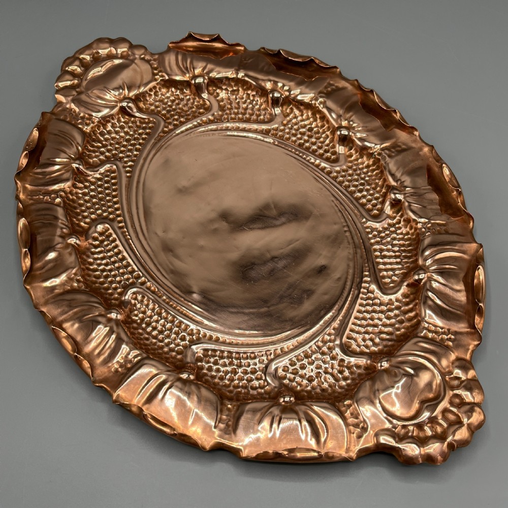 An oval Art Nouveau copper tray with hand-punched background texturing, scalloped edges, and embossed floral relief motifs. View X