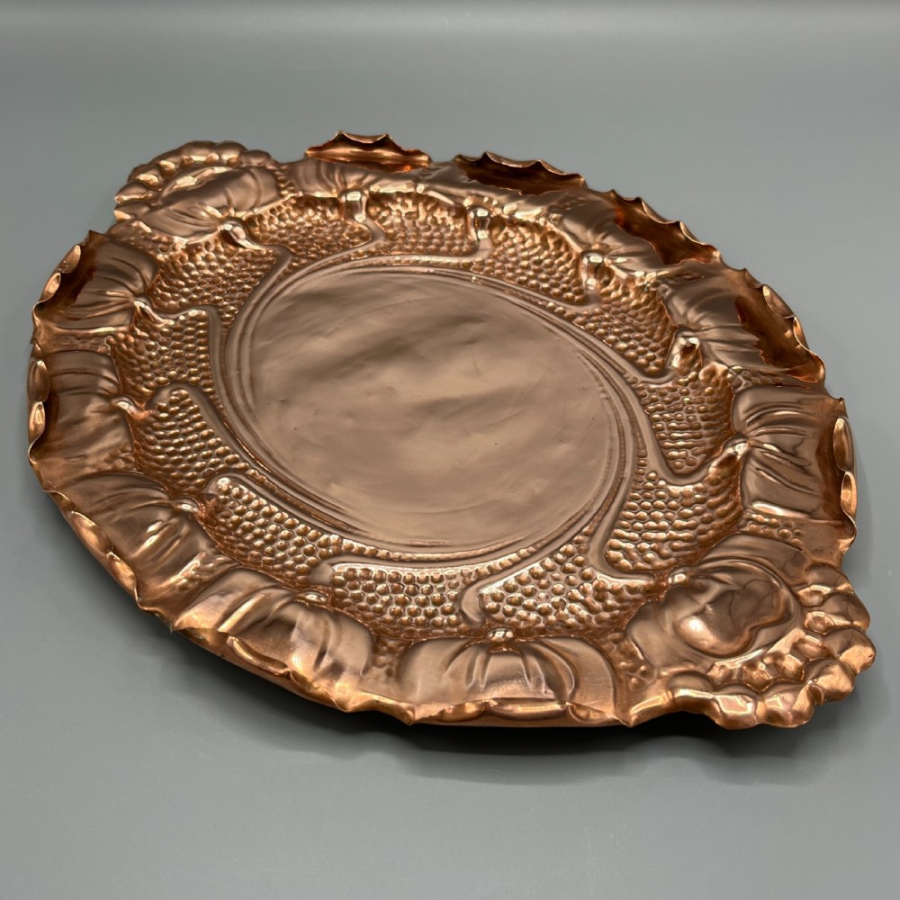 An oval Art Nouveau copper tray with hand-punched background texturing, scalloped edges, and embossed floral relief motifs. View XI