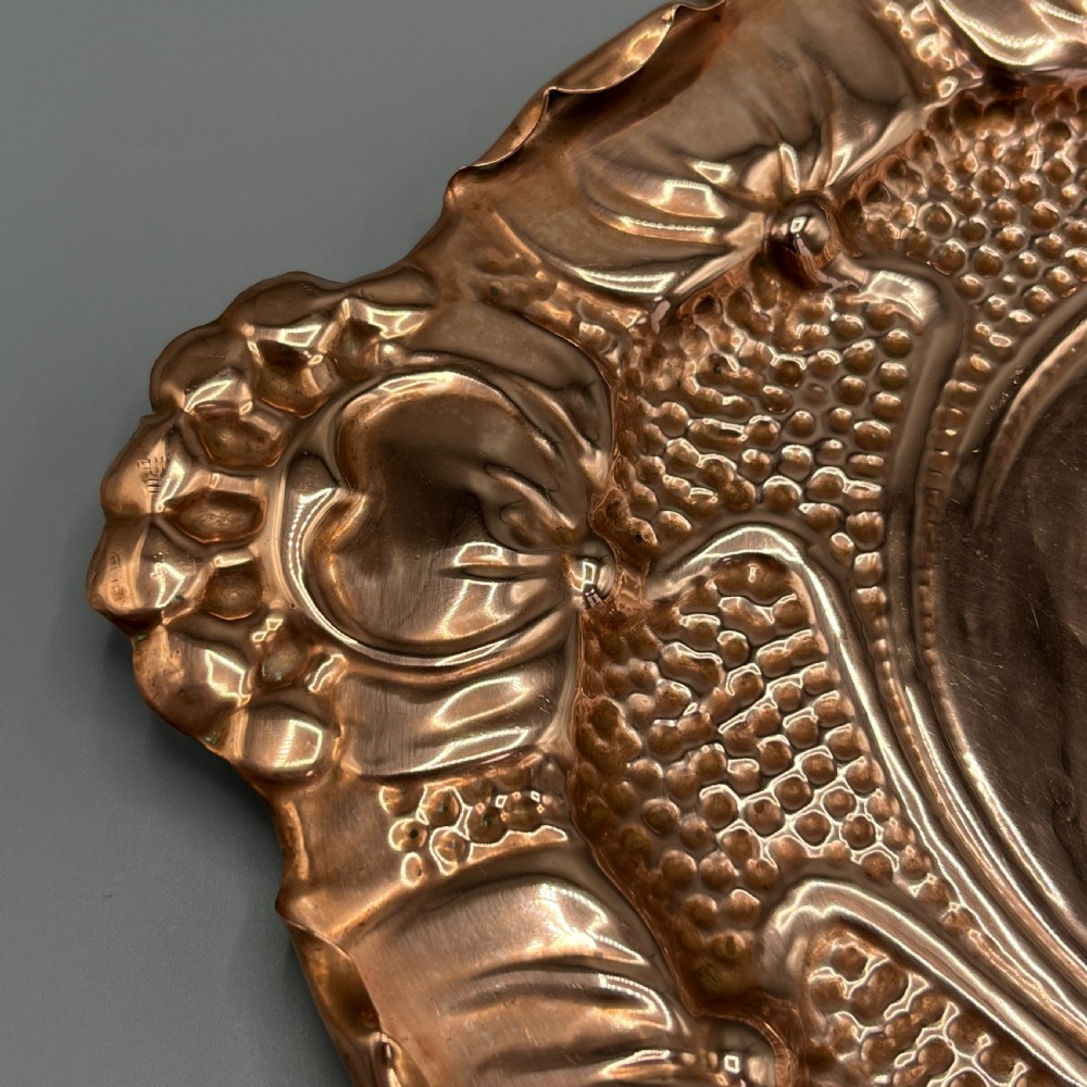 An oval Art Nouveau copper tray with hand-punched background texturing, scalloped edges, and embossed floral relief motifs. View XII