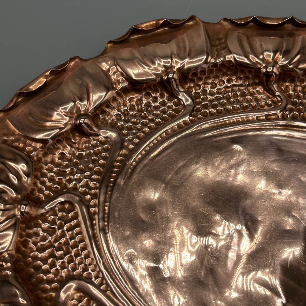 An oval Art Nouveau copper tray with hand-punched background texturing, scalloped edges, and embossed floral relief motifs. View XIII