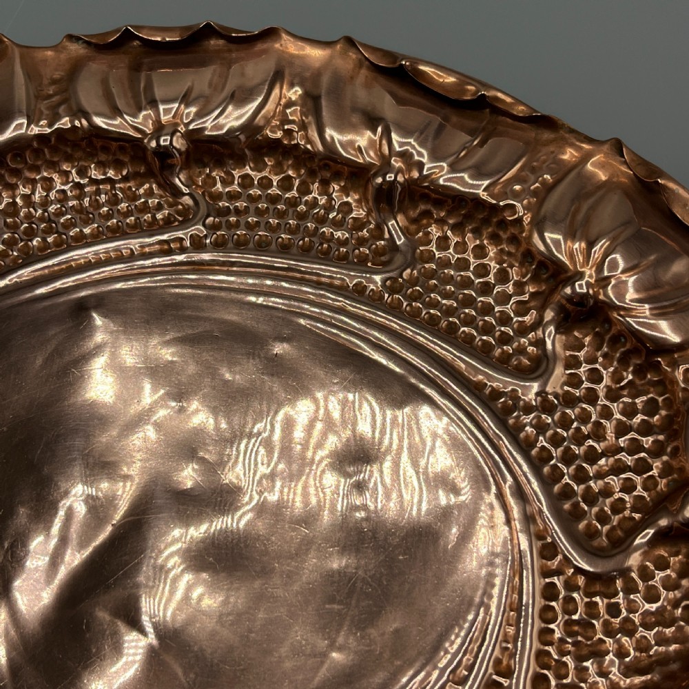 An oval Art Nouveau copper tray with hand-punched background texturing, scalloped edges, and embossed floral relief motifs. View XV