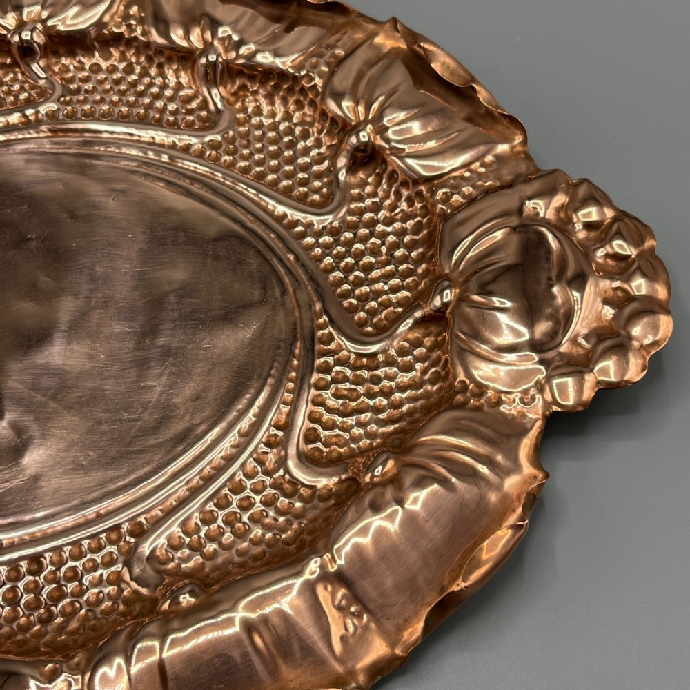 An oval Art Nouveau copper tray with hand-punched background texturing, scalloped edges, and embossed floral relief motifs. View XVI