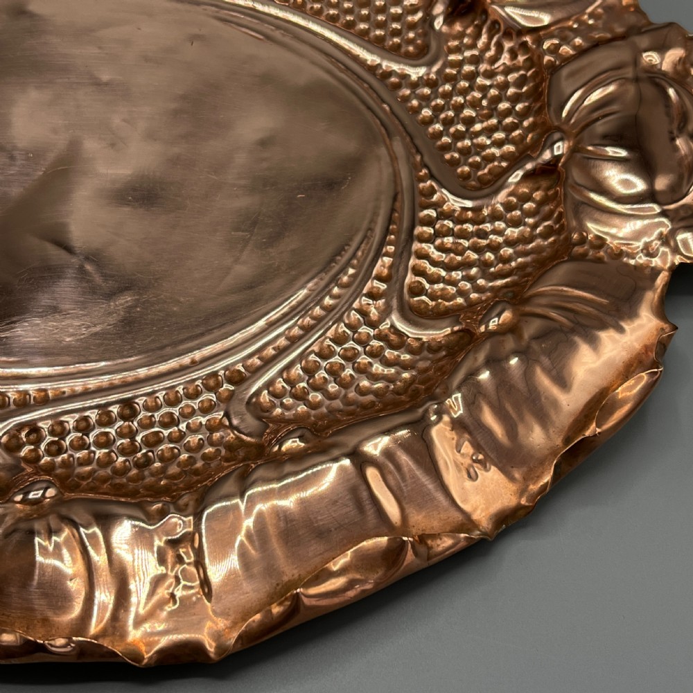 An oval Art Nouveau copper tray with hand-punched background texturing, scalloped edges, and embossed floral relief motifs. View XVII
