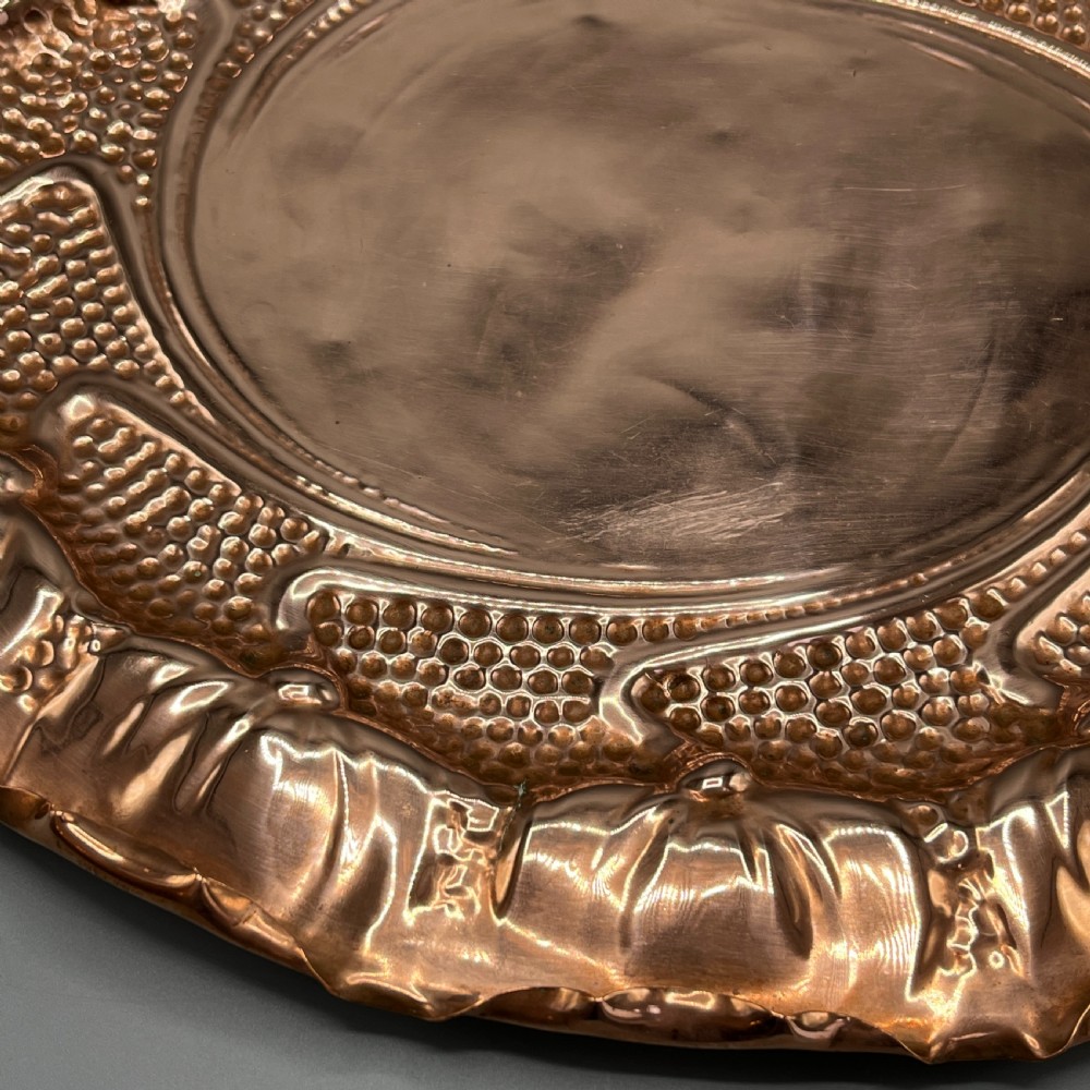 An oval Art Nouveau copper tray with hand-punched background texturing, scalloped edges, and embossed floral relief motifs. View XVIII