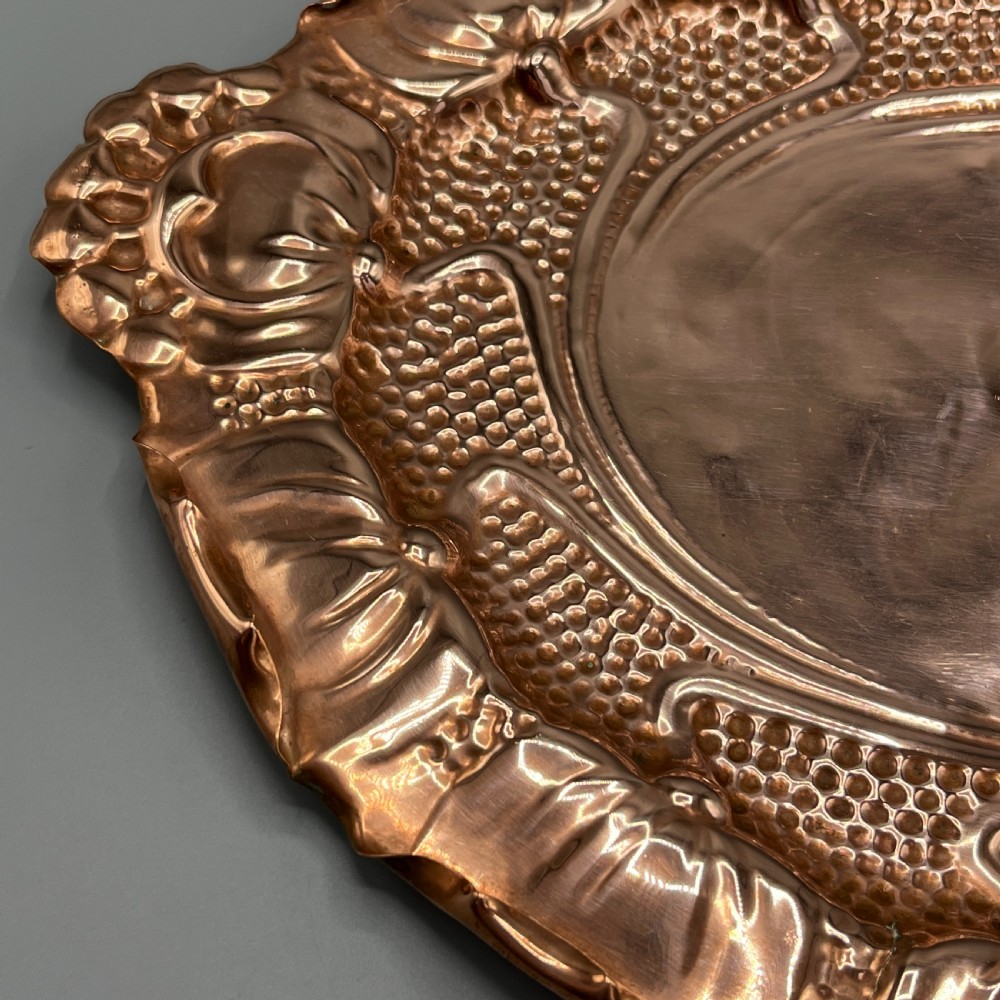 An oval Art Nouveau copper tray with hand-punched background texturing, scalloped edges, and embossed floral relief motifs. View XIX