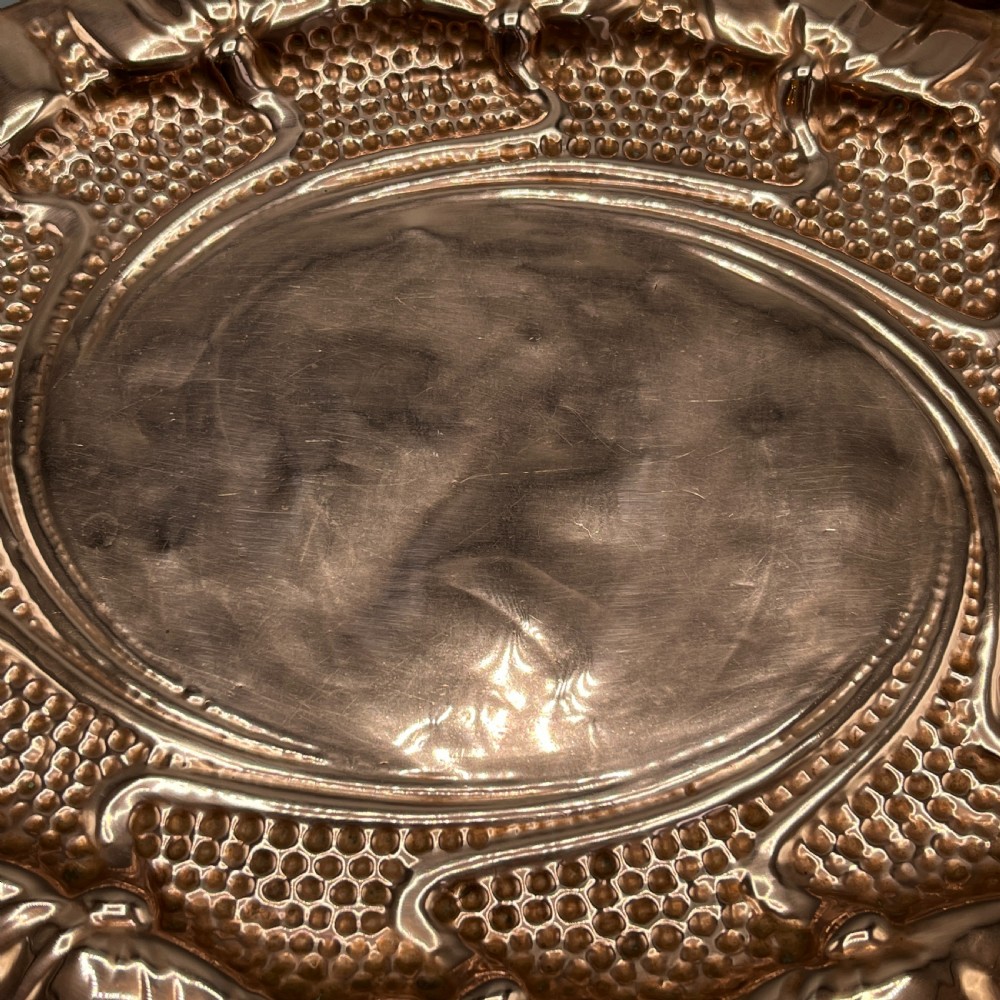 An oval Art Nouveau copper tray with hand-punched background texturing, scalloped edges, and embossed floral relief motifs. View XX