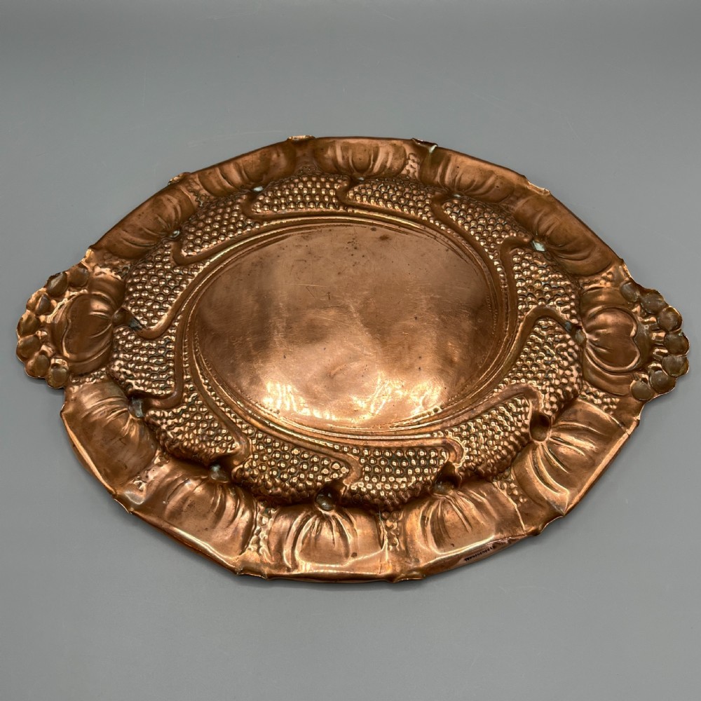 An oval Art Nouveau copper tray with hand-punched background texturing, scalloped edges, and embossed floral relief motifs. View XXI