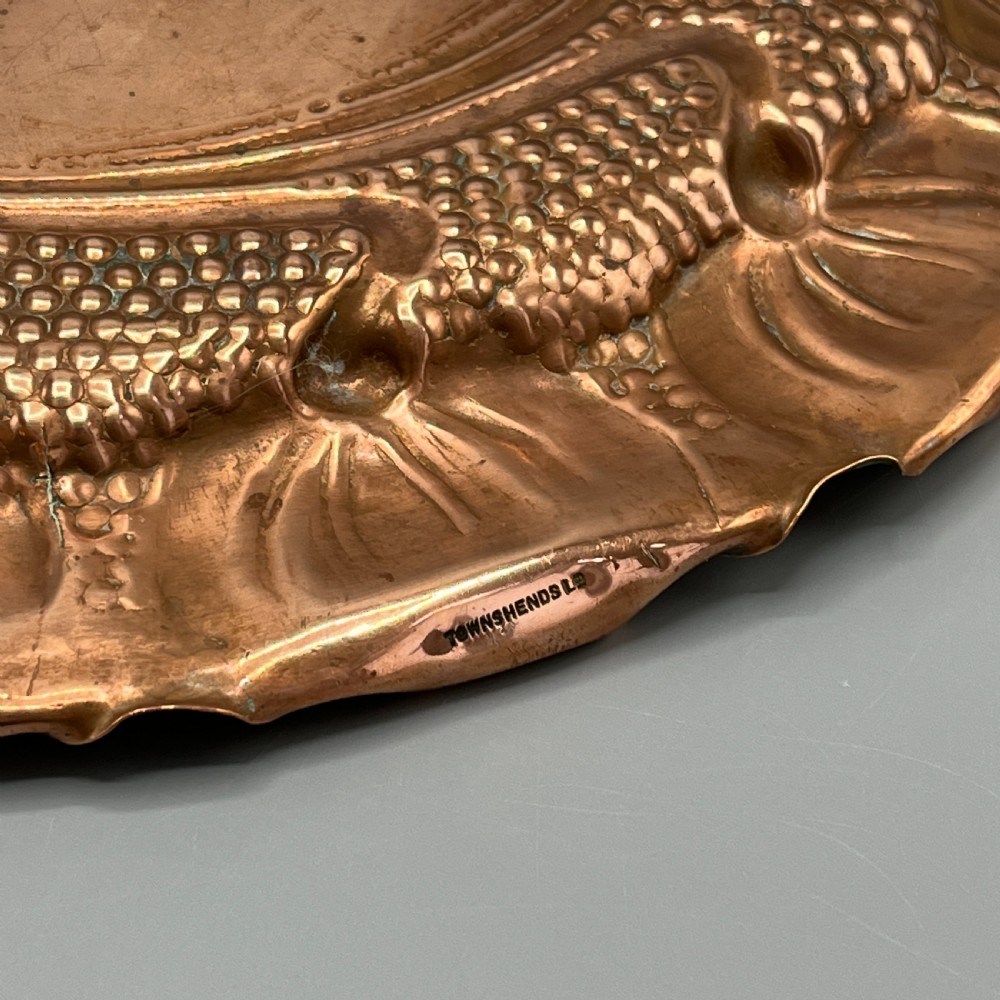 An oval Art Nouveau copper tray with hand-punched background texturing, scalloped edges, and embossed floral relief motifs. View XXII