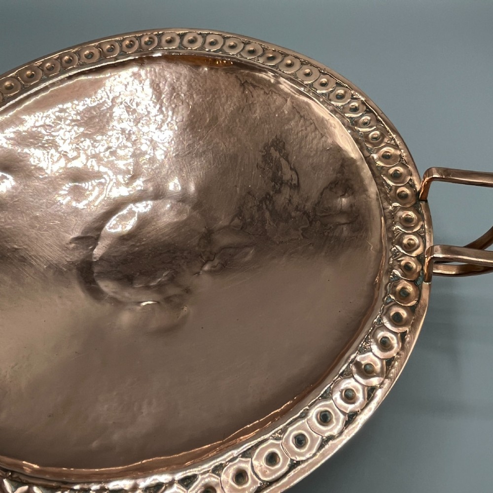 A hand-hammered copper tazza featuring twin side handles, a circular pedestal base, and a stamped geometric border along the shallow bowl rim. View VIII