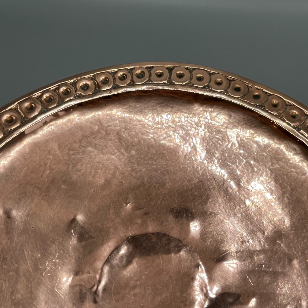 A hand-hammered copper tazza featuring twin side handles, a circular pedestal base, and a stamped geometric border along the shallow bowl rim. View IX