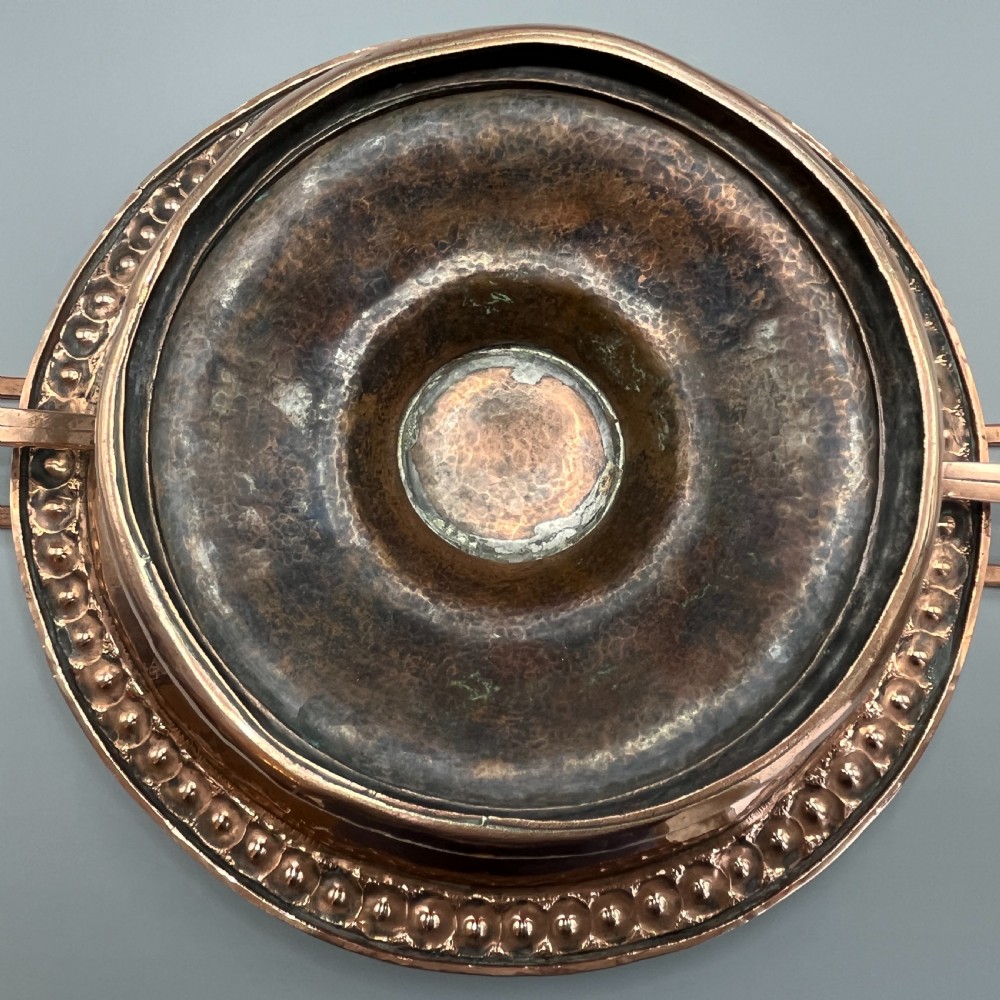 A hand-hammered copper tazza featuring twin side handles, a circular pedestal base, and a stamped geometric border along the shallow bowl rim. View XI