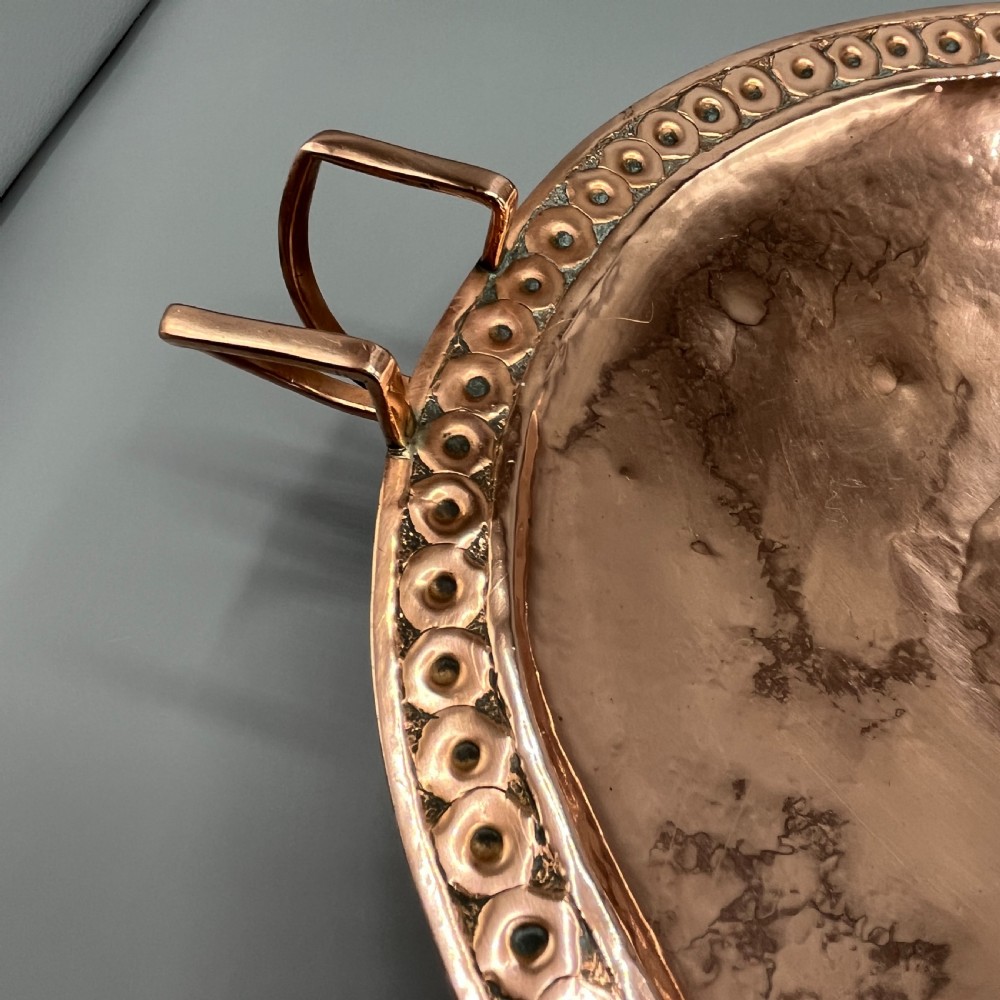 A hand-hammered copper tazza featuring twin side handles, a circular pedestal base, and a stamped geometric border along the shallow bowl rim. View XII