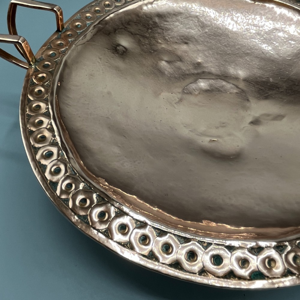A hand-hammered copper tazza featuring twin side handles, a circular pedestal base, and a stamped geometric border along the shallow bowl rim. View XIII