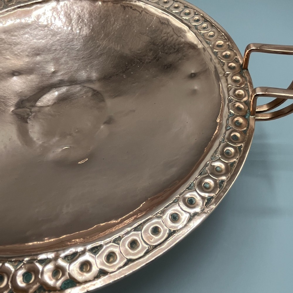 A hand-hammered copper tazza featuring twin side handles, a circular pedestal base, and a stamped geometric border along the shallow bowl rim. View XIV