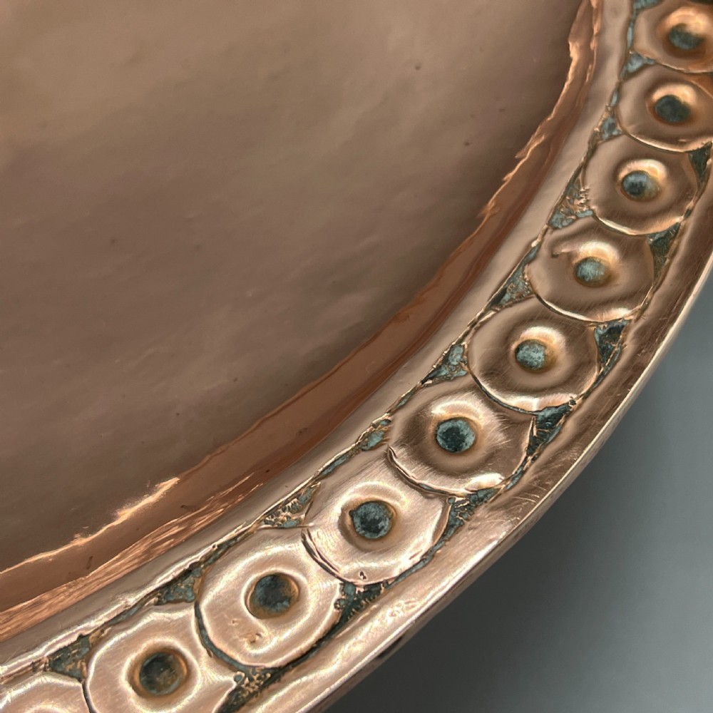 A hand-hammered copper tazza featuring twin side handles, a circular pedestal base, and a stamped geometric border along the shallow bowl rim. View XV