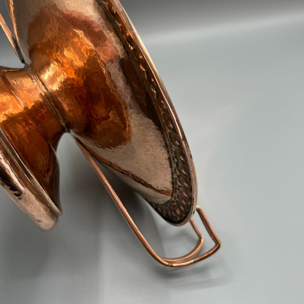 A hand-hammered copper tazza featuring twin side handles, a circular pedestal base, and a stamped geometric border along the shallow bowl rim. View XVII