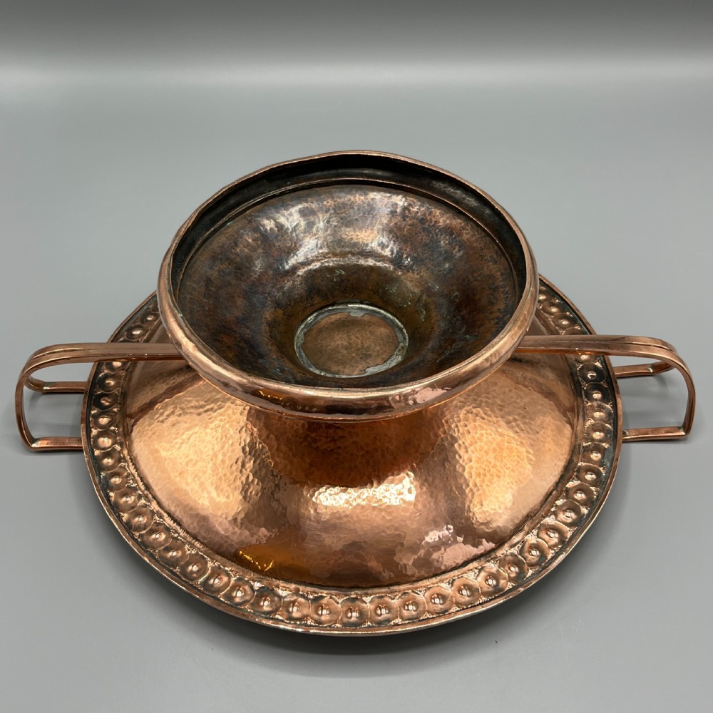 A hand-hammered copper tazza featuring twin side handles, a circular pedestal base, and a stamped geometric border along the shallow bowl rim. View XVIII
