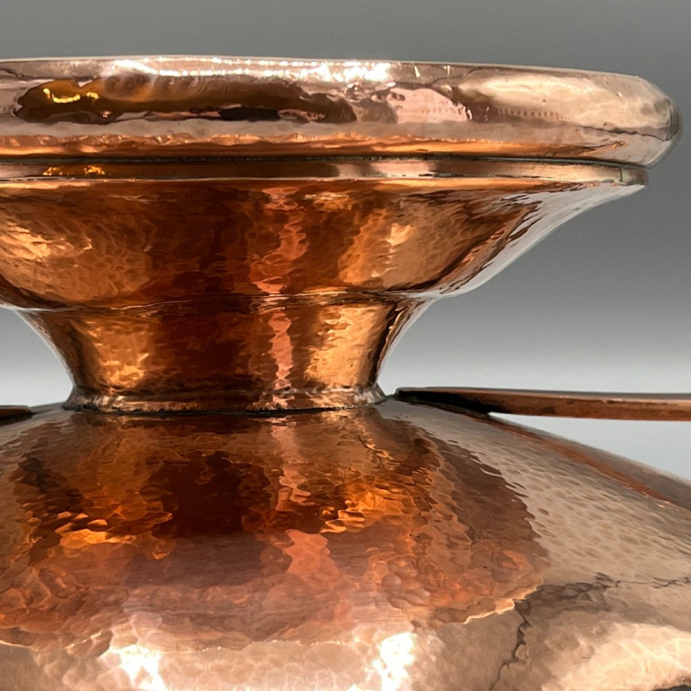 A hand-hammered copper tazza featuring twin side handles, a circular pedestal base, and a stamped geometric border along the shallow bowl rim. View XIX